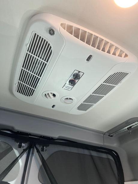 RV rental: Ceiling-mounted Coleman Mach air conditioner unit with multiple vents and control knobs for climate comfort.