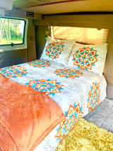 Cozy RV rental interior with a comfy bed, white and colorful mandala bedding, and a scenic window view.