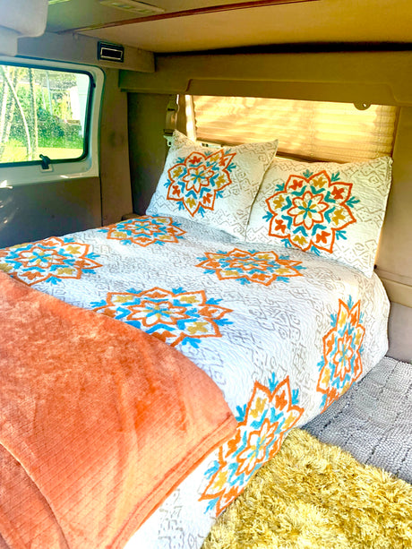 Cozy RV rental interior with a comfy bed, white and colorful mandala bedding, and a scenic window view.