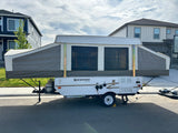 A Rockwood pop-up RV rental, fully set up with canvas sides, is parked on a street. Perfect for camping adventures.