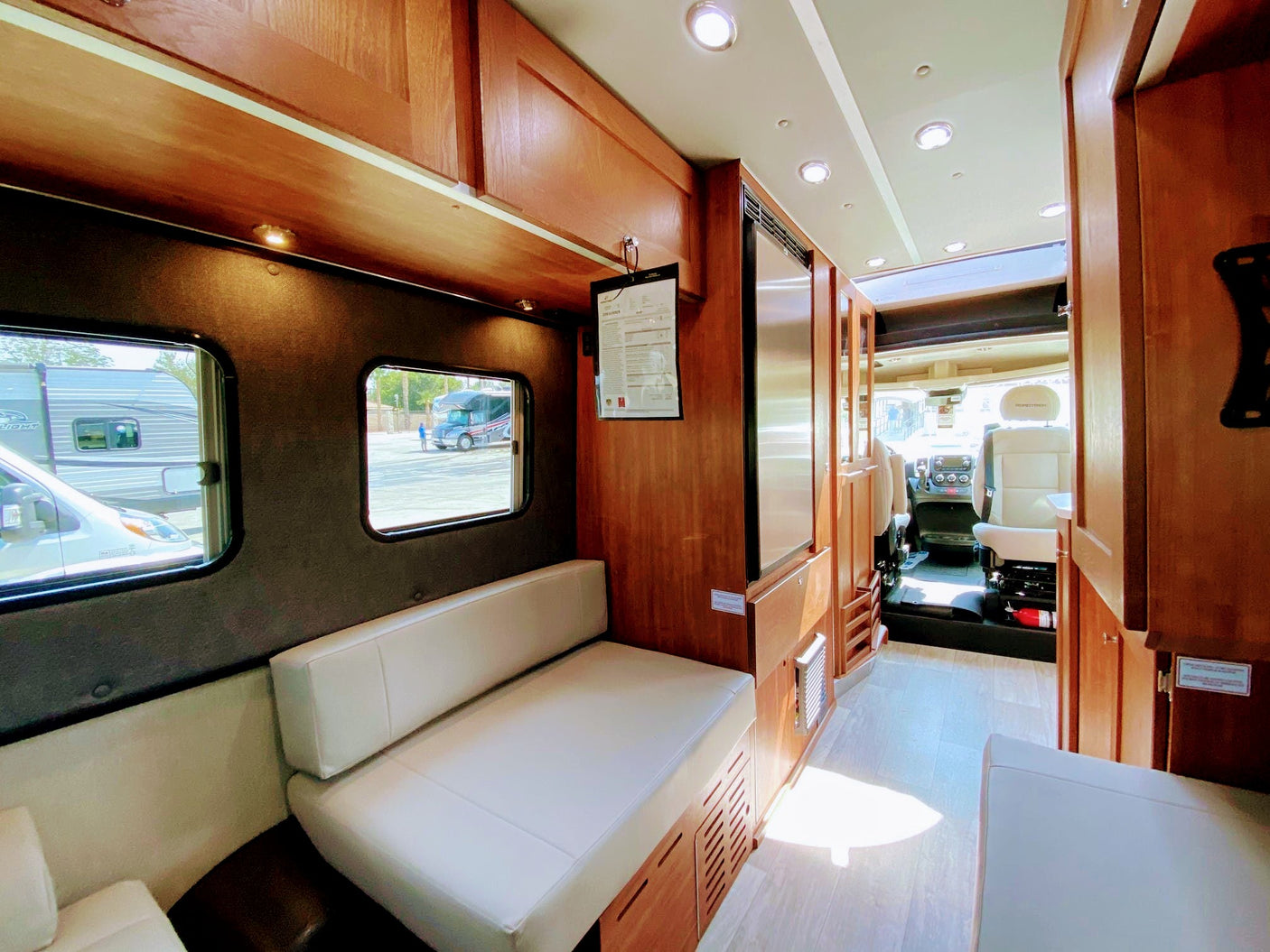 Inside this RV rental: a bright living space with light bench seating, wooden cabinets, and a clear view to the front.