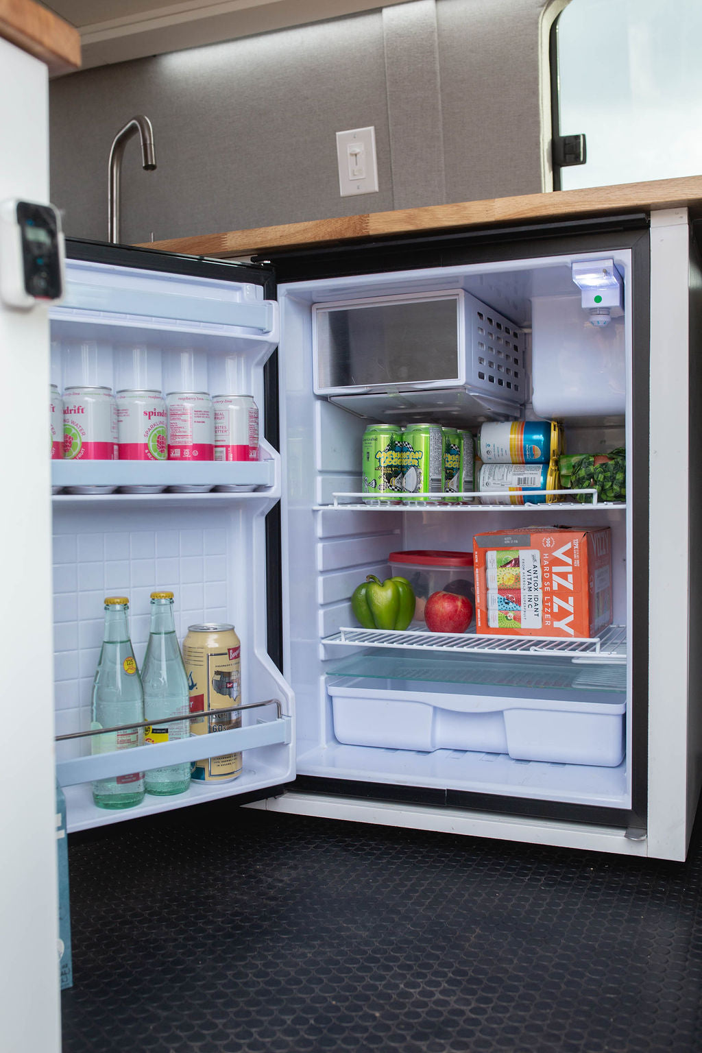 Compact RV rental fridge, well-stocked with drinks and fresh produce, perfect for road trips.
