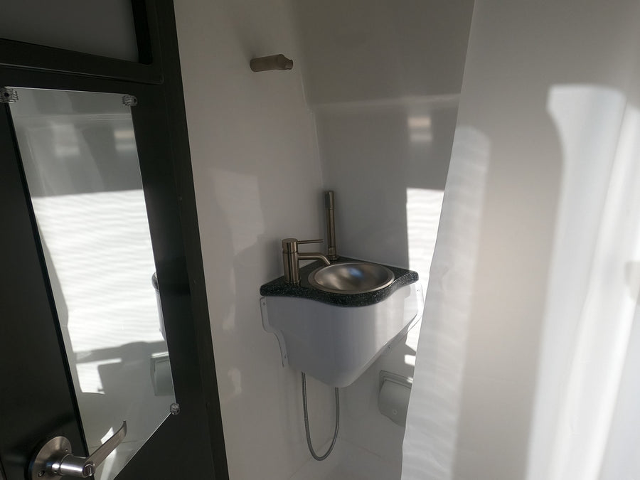 Compact RV rental bathroom: a small, shiny sink with modern faucet, next to a dark-framed door.