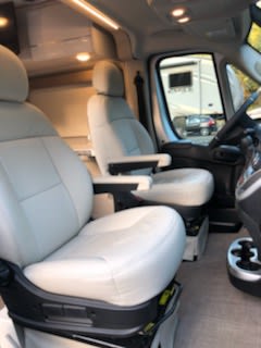 View inside an RV rental's front cabin, showcasing comfortable light-colored swivel captain's chairs for your journey. — photo 13