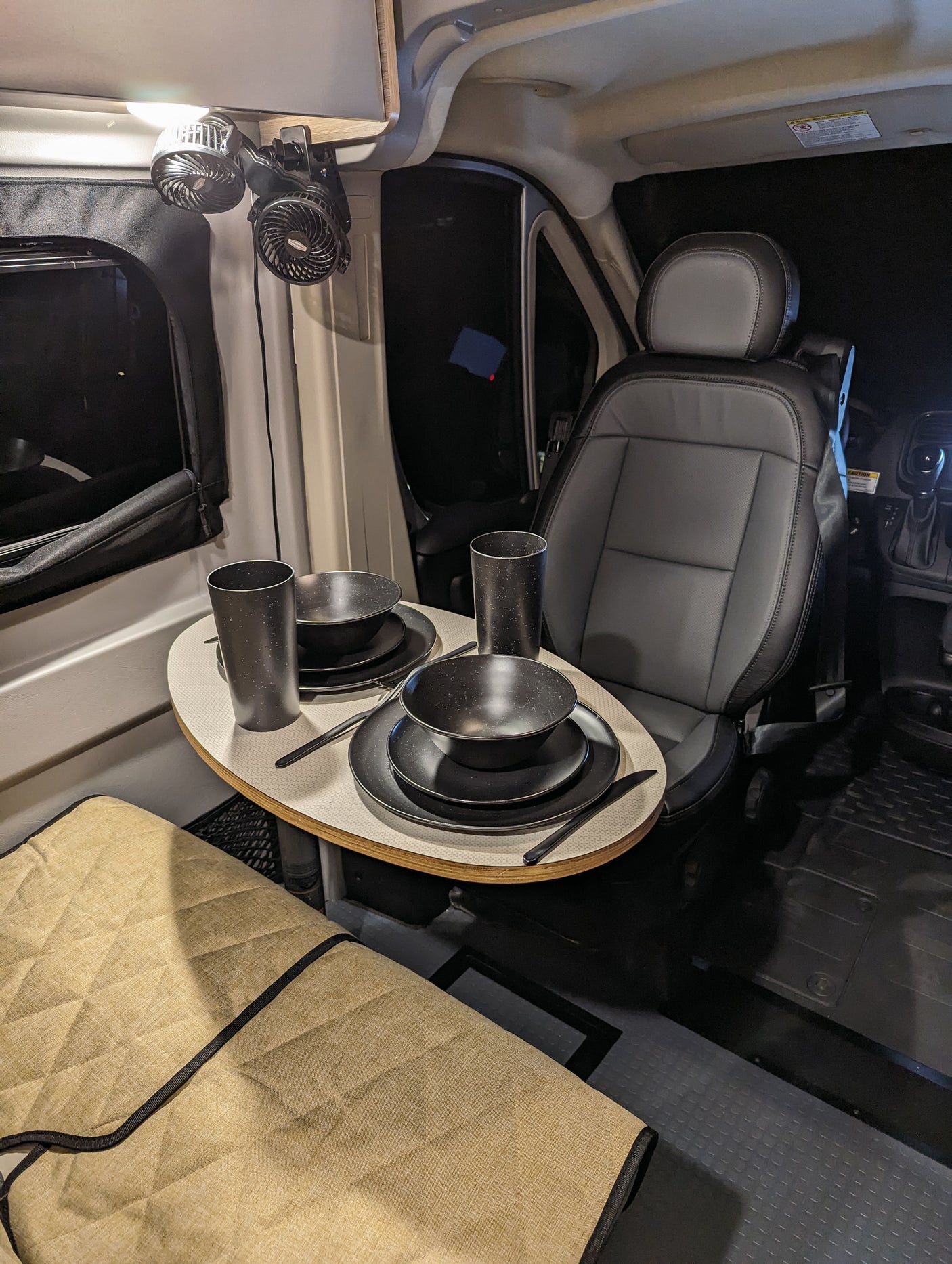 Inside this RV rental, a small dining table is set for two next to the driver's seat, with fans above.