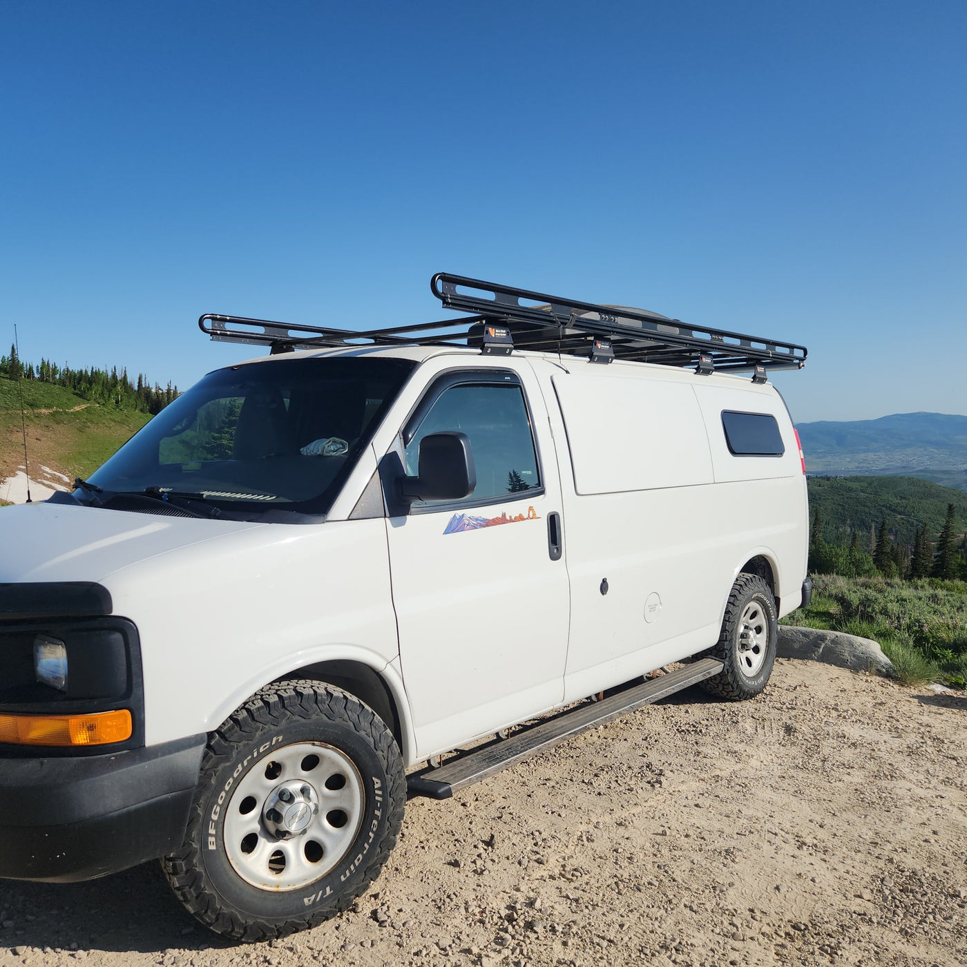 Scenic mountain view behind a white adventure camper van with roof rack, ready for your next rv rental journey. — photo 3