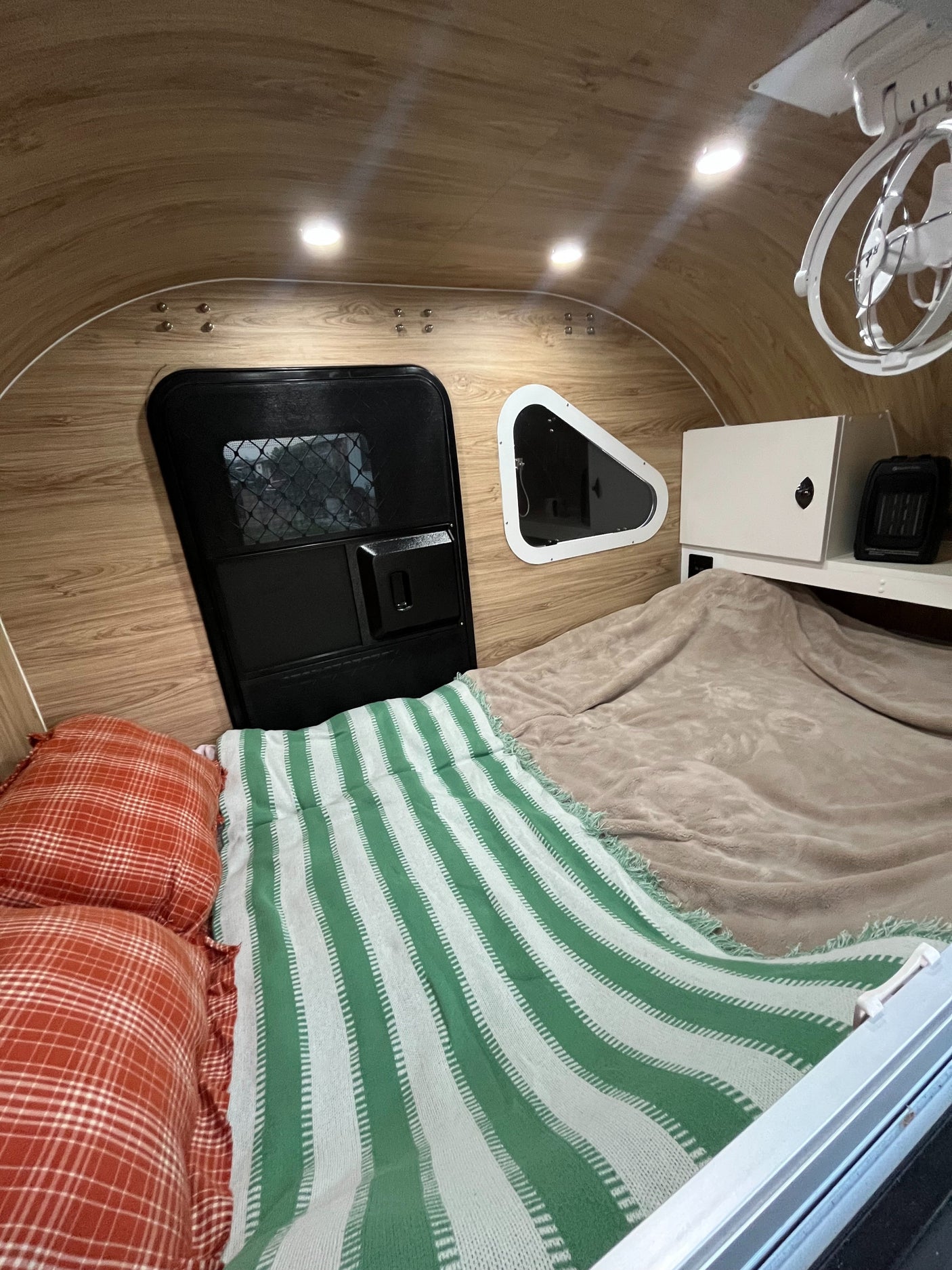 Cozy RV rental interior with bed, wood paneling, lights, and fan – perfect for travel.