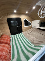 Cozy RV rental interior with bed, wood paneling, lights, and fan – perfect for travel.