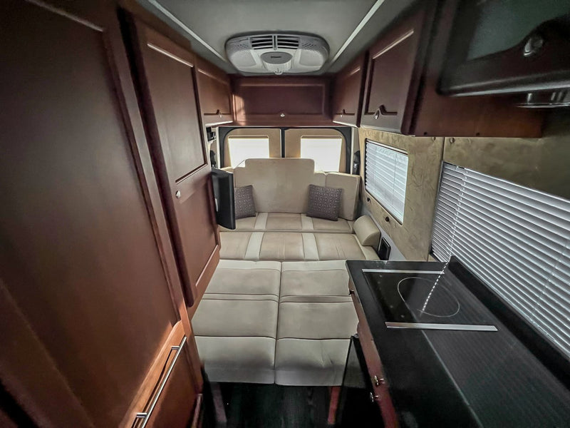 Experience luxury travel with this spacious rv rental interior, featuring a convertible lounge bed, modern kitchen, and rich wood cabinets. — photo 20