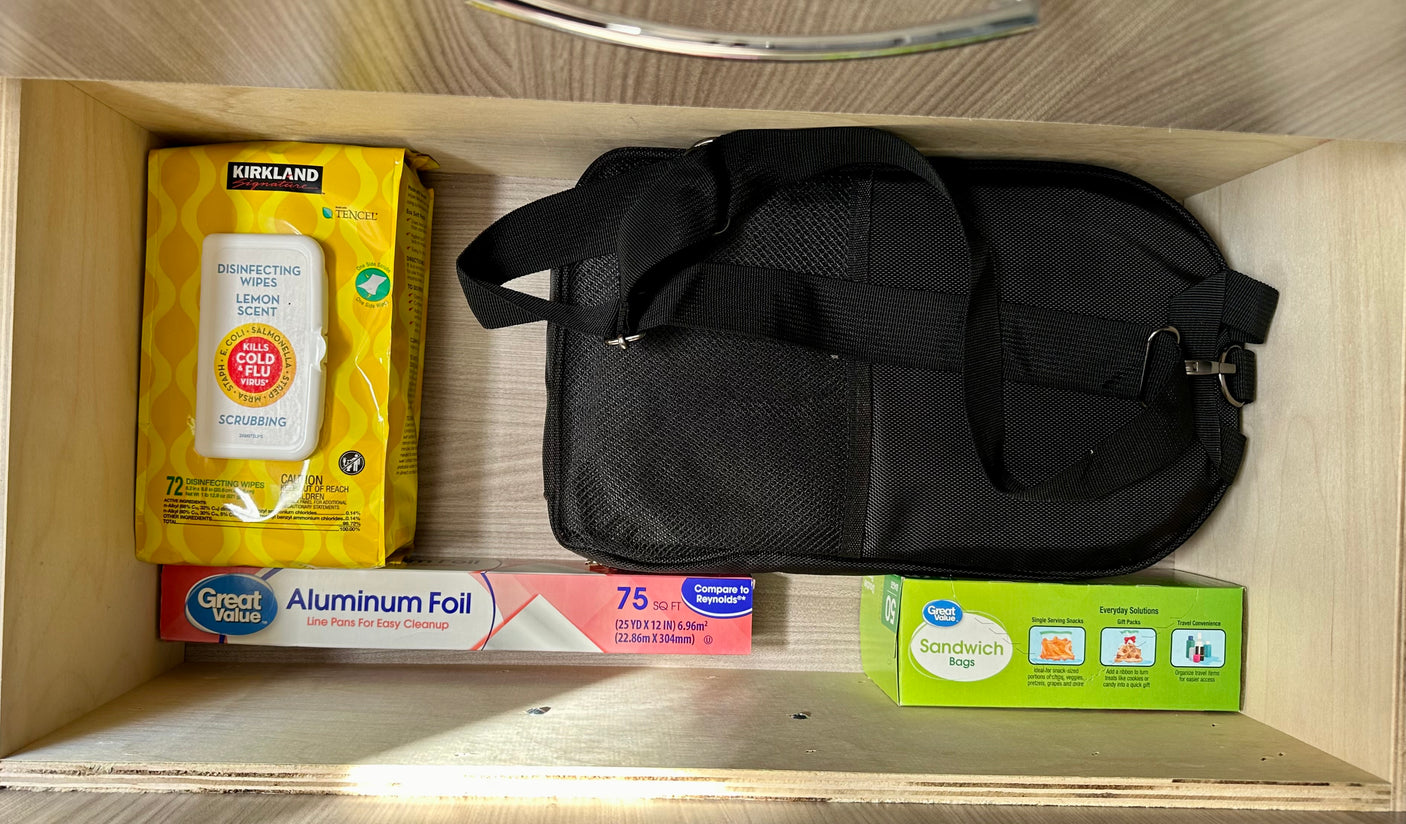 Organized RV rental drawer: disinfecting wipes, aluminum foil, sandwich bags & black bag for essentials.
