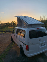 White Nissan NV200 camper van with pop-top extended at sunset, ready for an RV rental road trip in a tropical setting.