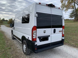 Rear view of a white Ram ProMaster camper van, ideal for RV rental. Parked on a rural gravel road.