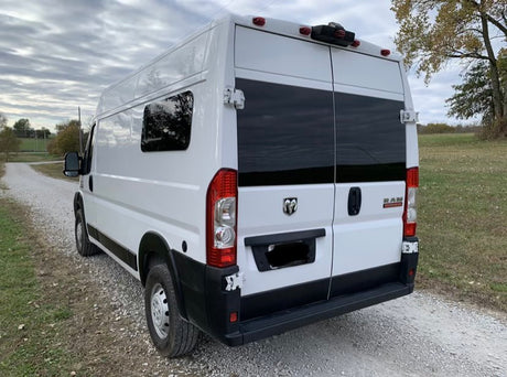 Rear view of a white Ram ProMaster camper van, ideal for RV rental. Parked on a rural gravel road.