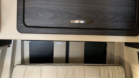 This RV rental features a dark wood cabinet, a comfortable cushioned seat, and an EXIT sign visible on a window panel.