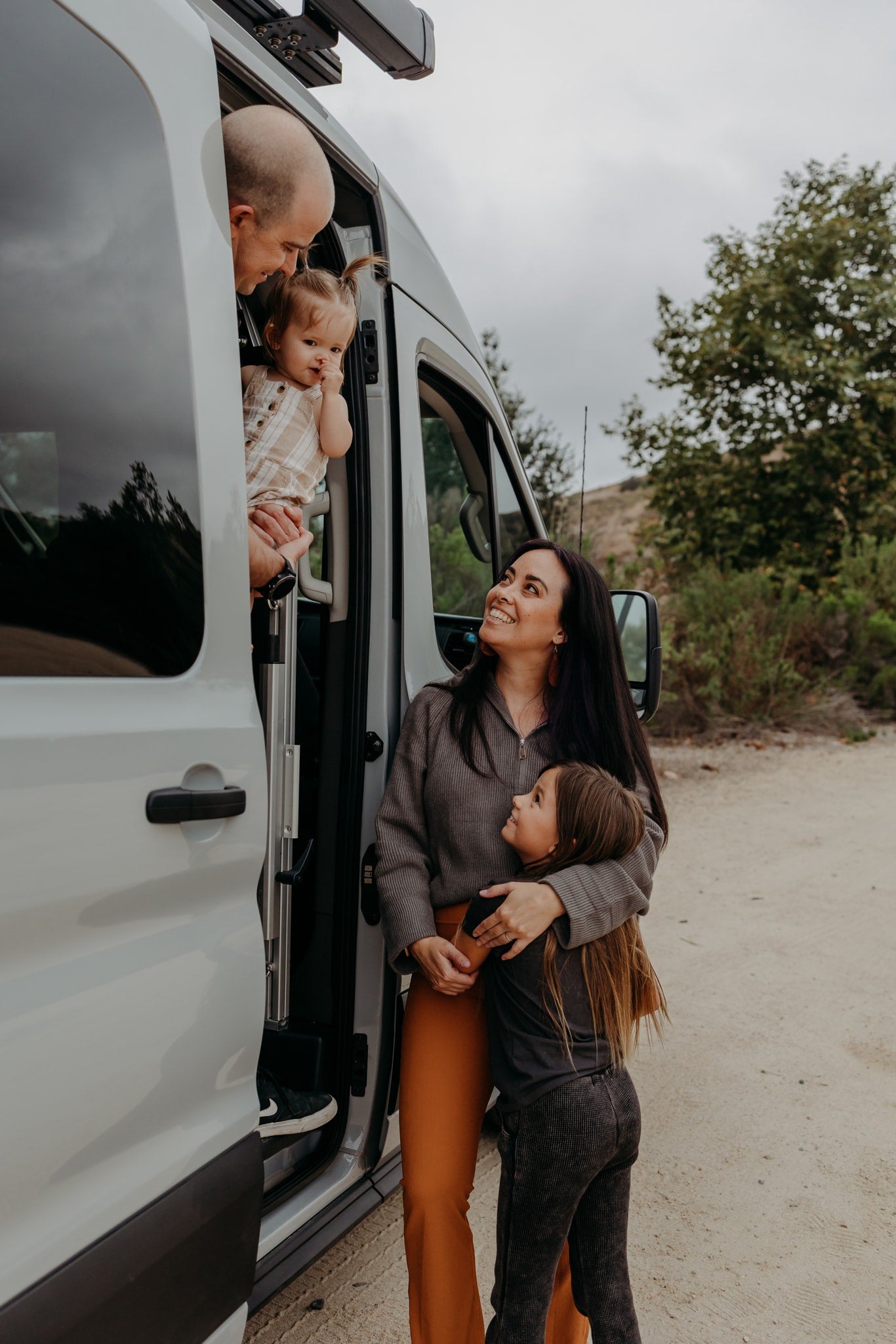 A joyful family outside their RV rental van. Dad holds baby at window, mom smiles with daughter. Embracing travel moments! — photo 11