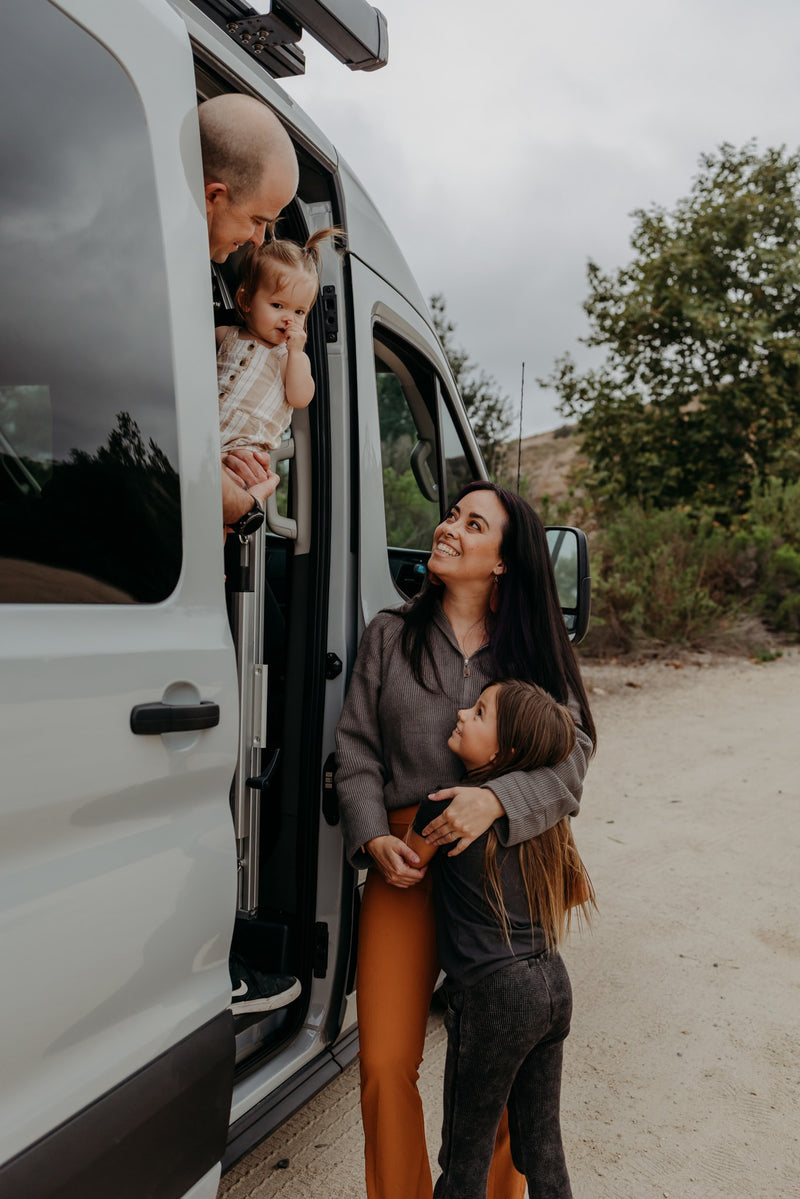 A joyful family outside their RV rental van. Dad holds baby at window, mom smiles with daughter. Embracing travel moments! — photo 11