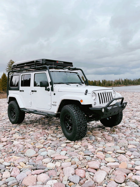 White Jeep Wrangler, iKamper rooftop tent on rocky riverbed. Overlanding ready! Explore unique rv rental options for adventure.