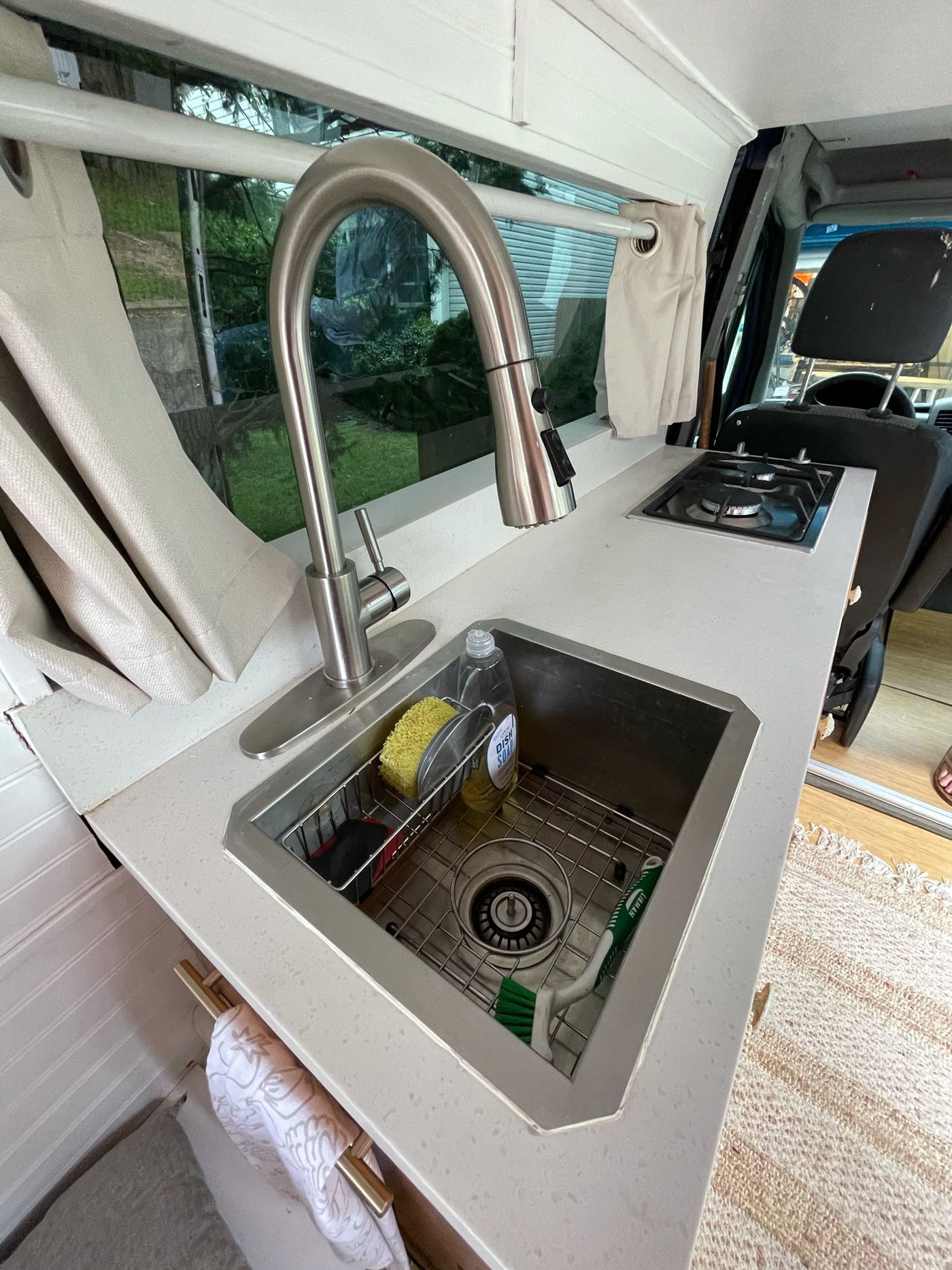 Compact RV rental kitchen features a sink, cooktop, and white counter in a functional van conversion setup. — photo 9