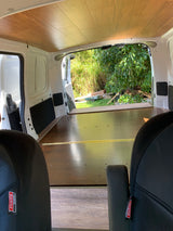 Interior of an RV rental van, featuring wood-paneled ceiling & floor, and open doors revealing a green outdoor scene.