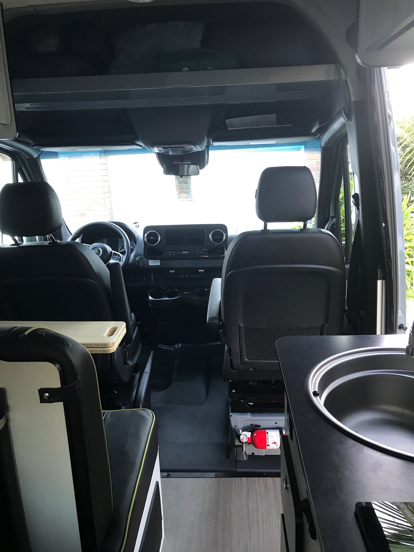 Inside an RV rental: view from rear showing driver's cockpit, seating, and a compact kitchen area with sink & fire extinguisher.