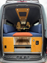 RV rental camper van interior. Rear view shows blue cushioned benches, wood accents, and practical storage drawers. Ready for adventure!