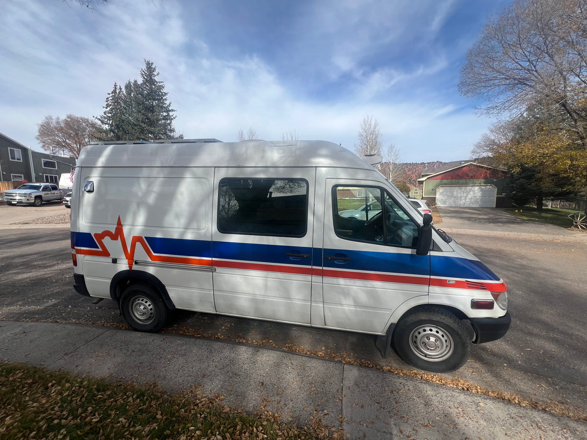 White Sprinter-style van with blue/red ECG stripe, possibly a custom rv rental, parked on a fall street. — photo 7