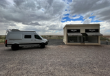 This RV rental (Winnebago Revel) is parked at Prada Marfa, a unique art installation in the desert under a cloudy sky.