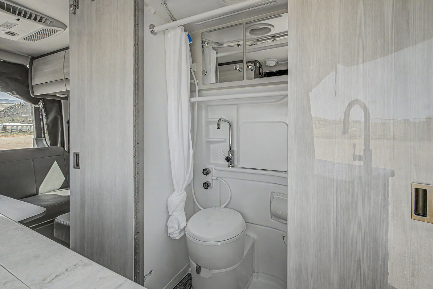 RV rental's modern wet bath: a compact toilet, shower, and sink faucet. Clean grey and white interior design.
