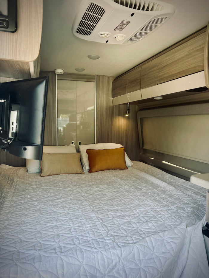 Modern RV rental bedroom featuring a large, inviting bed, TV, and overhead AC, ensuring comfortable travel stays.