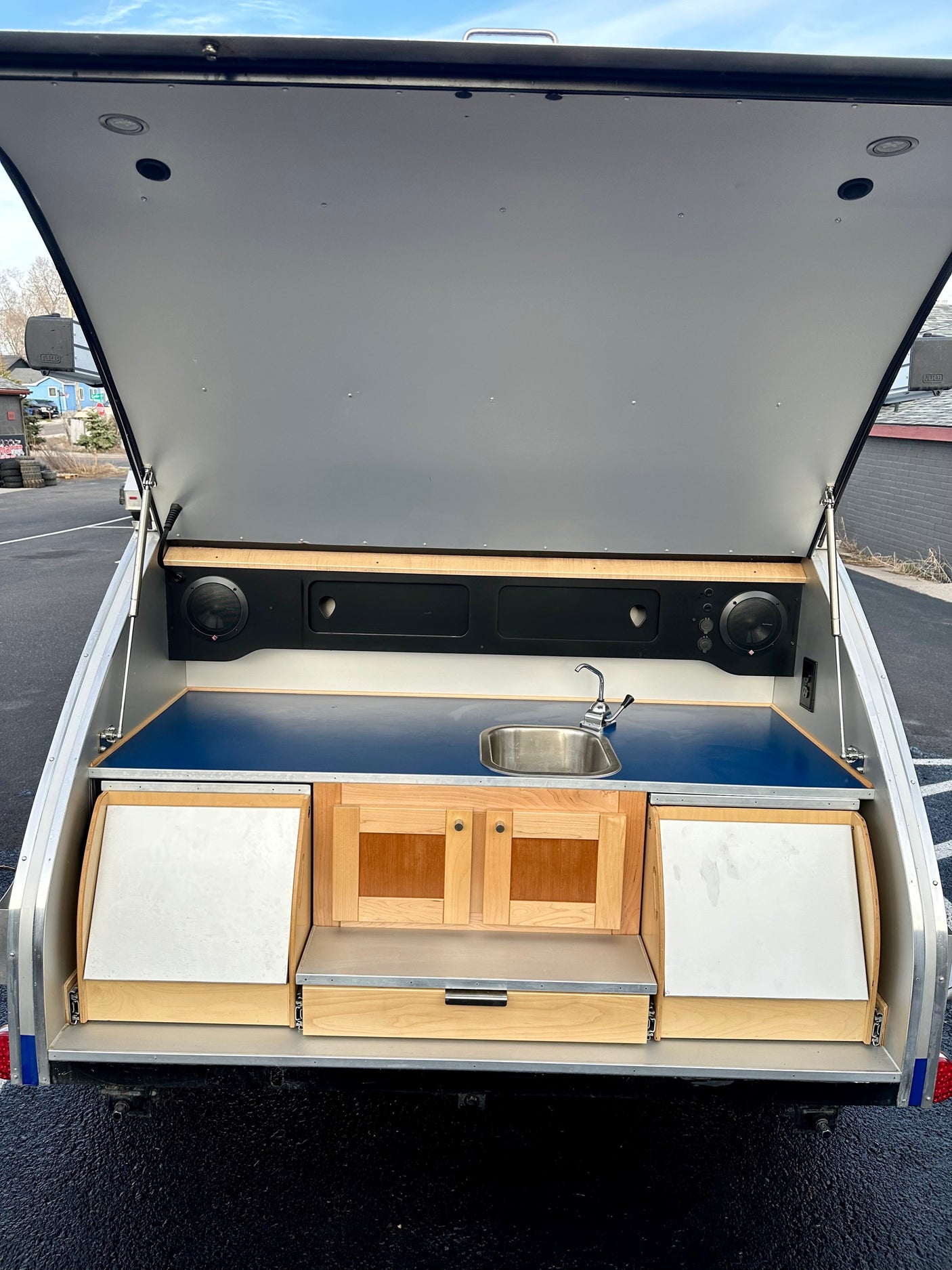 This RV rental teardrop trailer shows its open rear hatch revealing a full outdoor kitchen with sink, cabinets, and speakers.