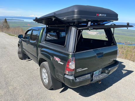 Dark green Toyota Tacoma pickup with an open iKamper rooftop tent, ideal for an RV rental exploring Alaska's scenic views.