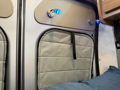 RV rental interior: illuminated blue reading lights, padded window cover, & overhead cabinet detail.