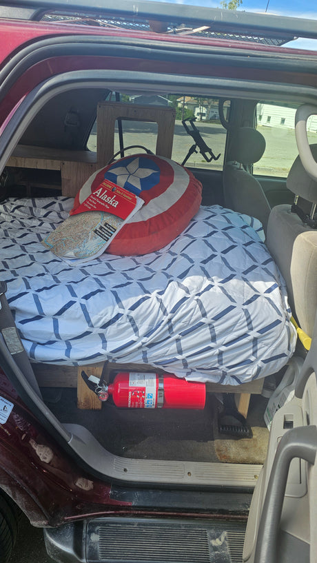 This DIY camper conversion for an RV rental features a bed, Captain America pillow, Alaska map, and fire extinguisher for safe travel.