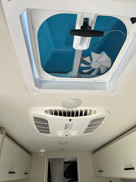 Looking up inside an RV rental: Features a ceiling vent with fan, air conditioning unit, and overhead storage cabinets.
