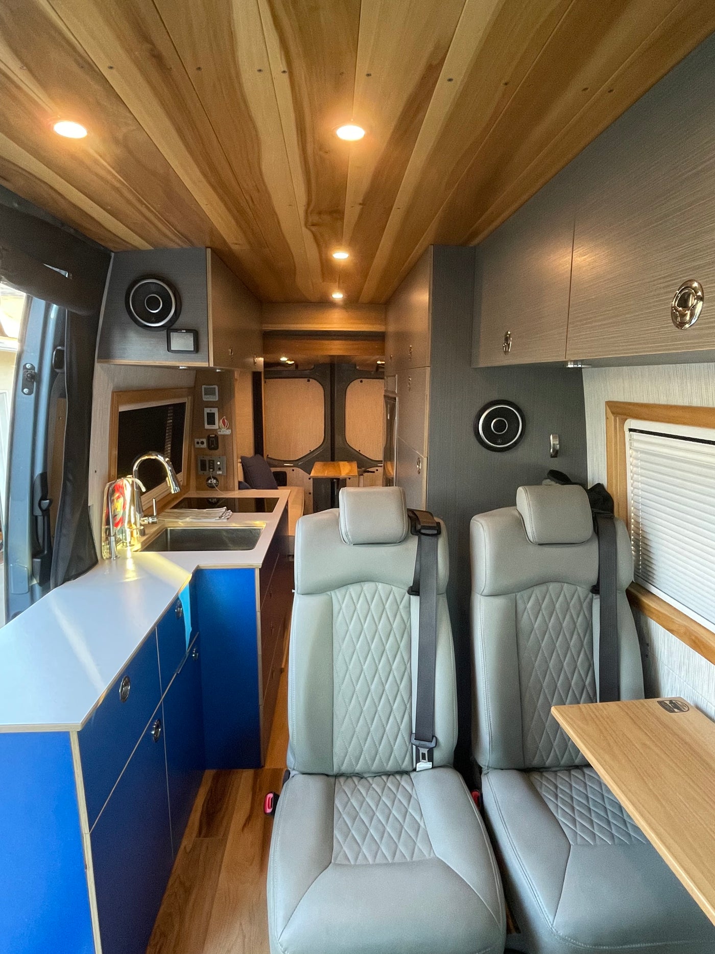 Step inside this stylish RV rental van conversion, featuring cozy gray seating, a vibrant blue kitchenette, and warm wooden ceilings. — photo 3