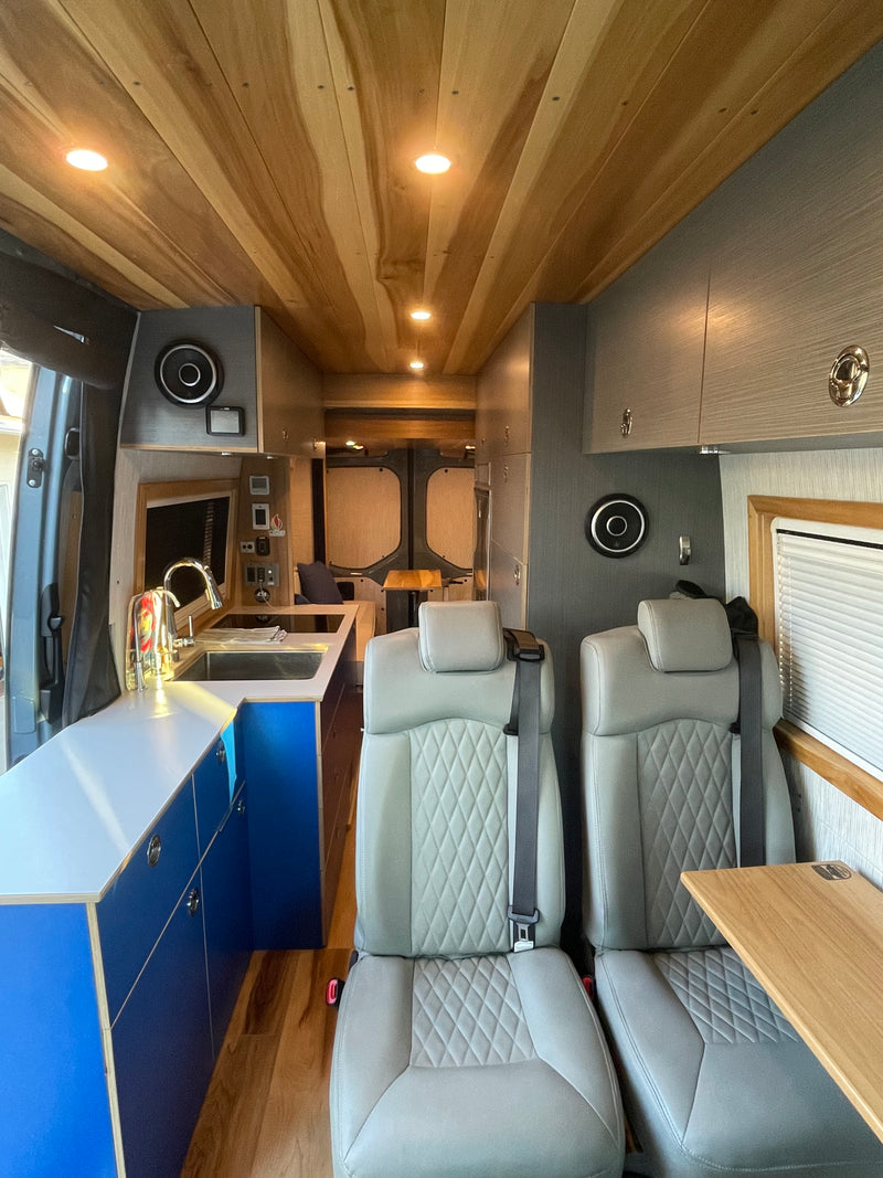 Step inside this stylish RV rental van conversion, featuring cozy gray seating, a vibrant blue kitchenette, and warm wooden ceilings. — photo 3