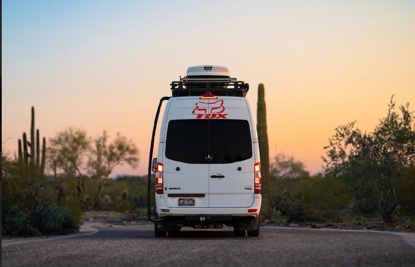 A white Mercedes Sprinter camper van, ideal for rv rental adventures, on a desert road at sunset with saguaro cacti.