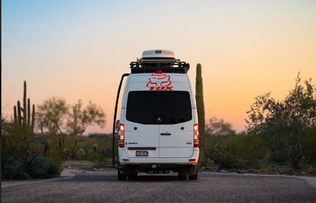 A white Mercedes Sprinter camper van, ideal for rv rental adventures, on a desert road at sunset with saguaro cacti.