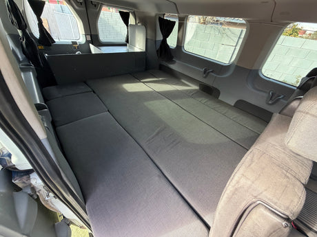 Interior view of an rv rental: a grey modular bed fills the campervan, with a small kitchenette at the back and privacy curtains.