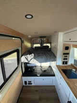 Inside a modern **rv rental**: a comfy bed, functional kitchenette, and control panel for ultimate road trip comfort.