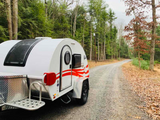 Explore nature with this small white teardrop RV rental on a winding gravel road through a serene forest.