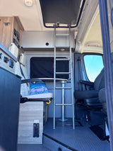 Interior of an RV rental: a ladder to the pop-top bed, textured floor, comfortable seating, and visible control panels.