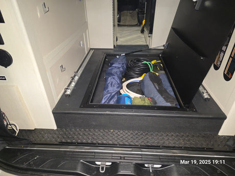 RV rental interior: an open floor storage hatch reveals coiled hoses, bags, and other essential gear for the road.