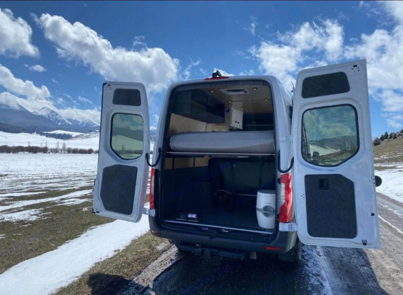  and large windows revealing a beautiful snowy landscape.|This RV rental features a flexible bench seating/bed area with storage & a compact kitchen with sink and fridge.|White **rv rental** camper van in a snowy mountain landscape. Its open rear reveals a cozy bed and storage within.|A white RV rental van illuminated under vibrant purple/green aurora — photo 10