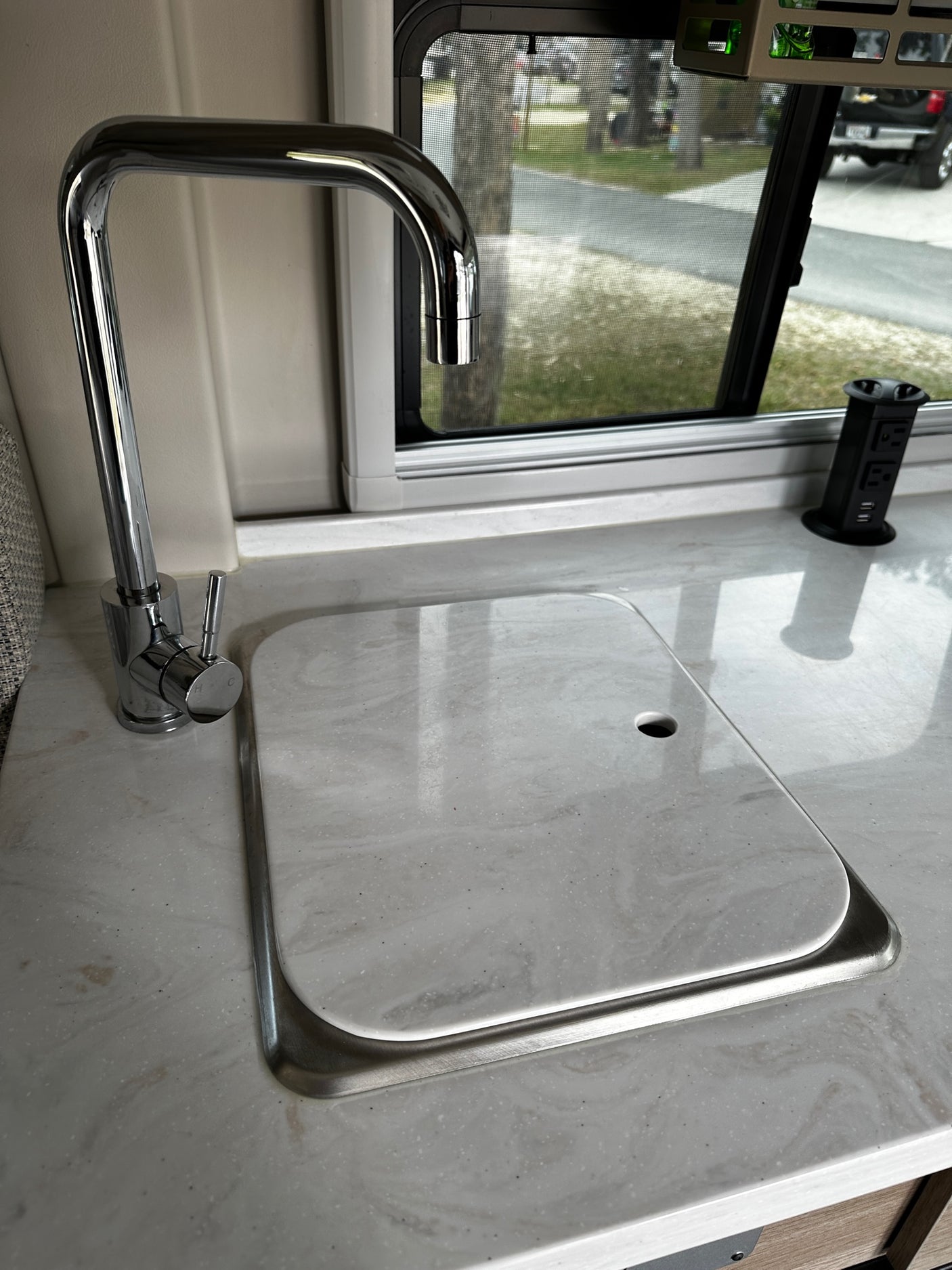 RV rental interior: Modern kitchen with a covered sink, pull-up outlet, and window view.