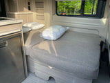 This RV rental offers a compact, functional interior with a convertible bed, kitchenette with fridge, and storage.