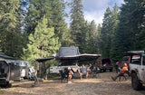 Friends gather at a forest camp, equipped with a robust RV rental trailer, ready for overlanding adventures.