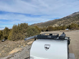 Sherpa Trailers rv rental: A white teardrop trailer with Curt cargo basket & rooftop awning, amidst arid mountains.