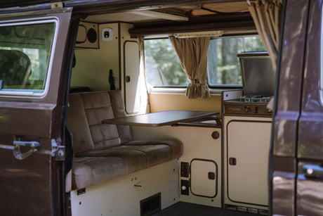 Cozy interior of an RV rental: brown bench seat, foldable table, and compact kitchen. Ready for your next road trip adventure!
