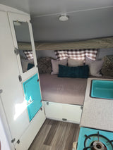 RV rental: Cozy camper interior, featuring a bed with pillows, teal sink, and stove setup.